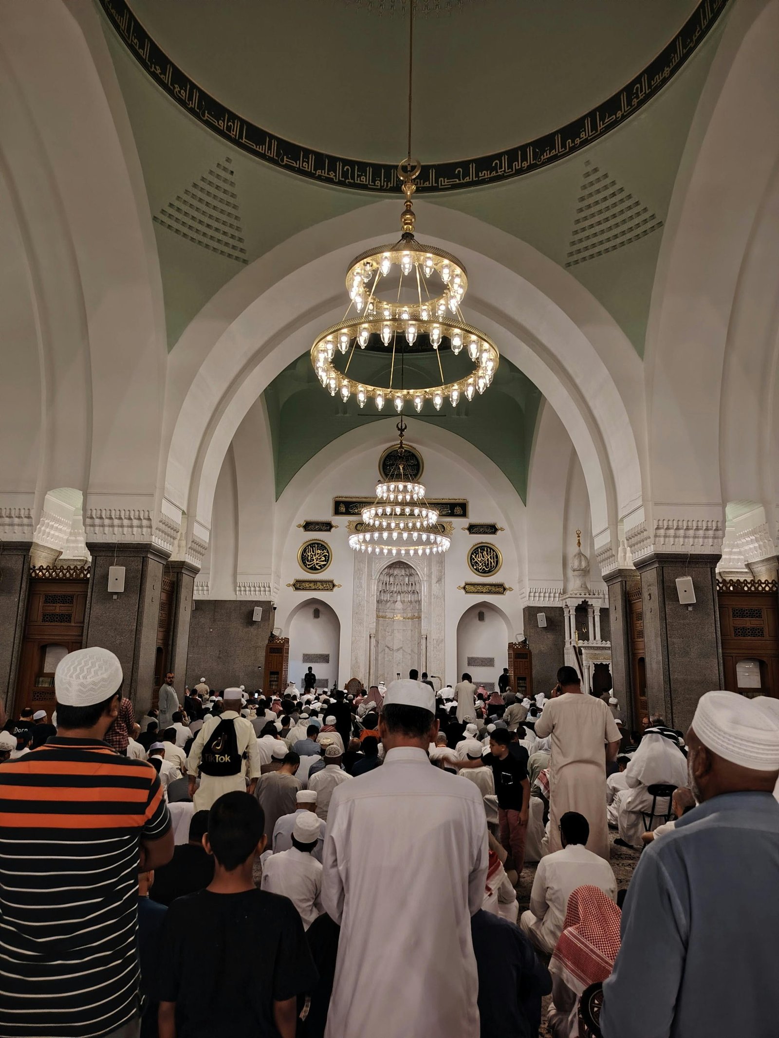 A gathering of worshippers inside a beautifully lit mosque during prayer time.