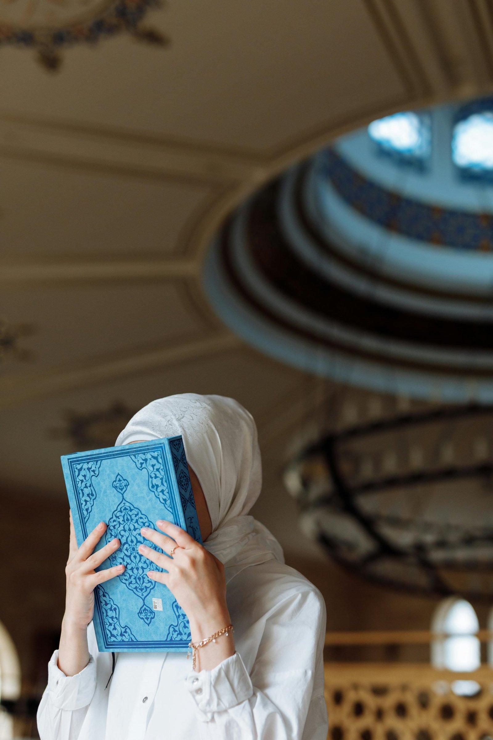 A woman in a hijab holding a blue book in a mosque, depicting devotion.
