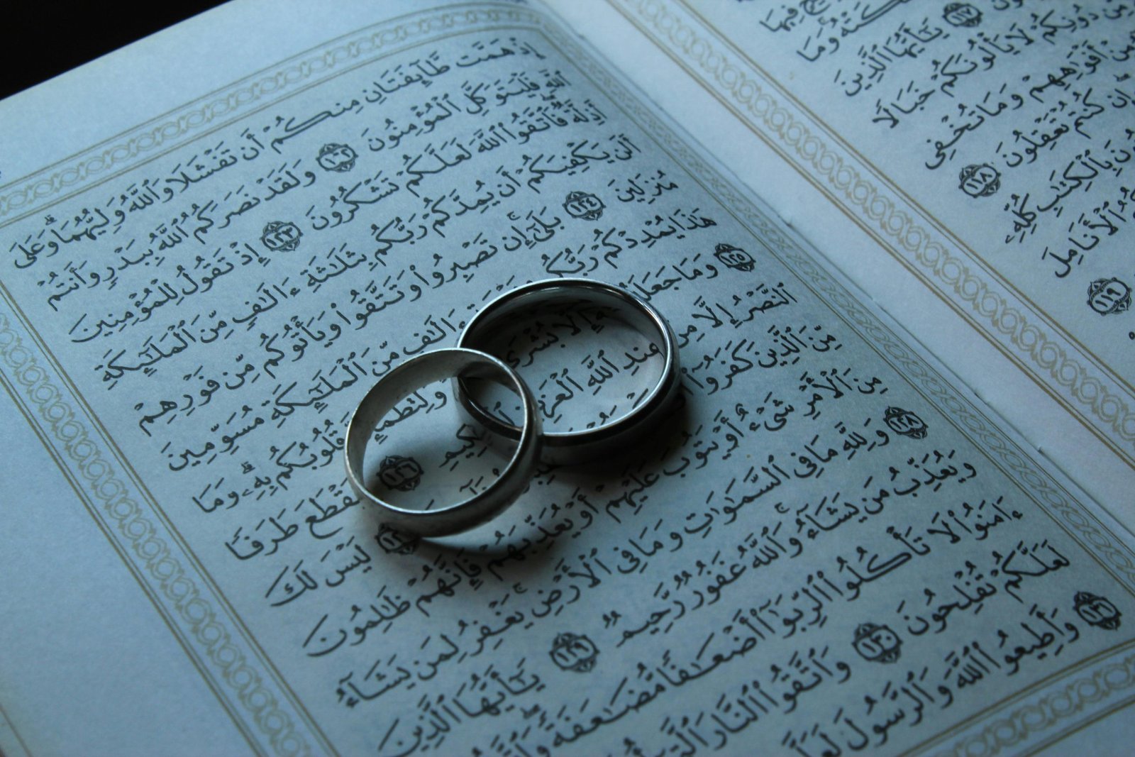Close-up of silver wedding rings on an open Quran page, symbolizing marriage and spirituality.