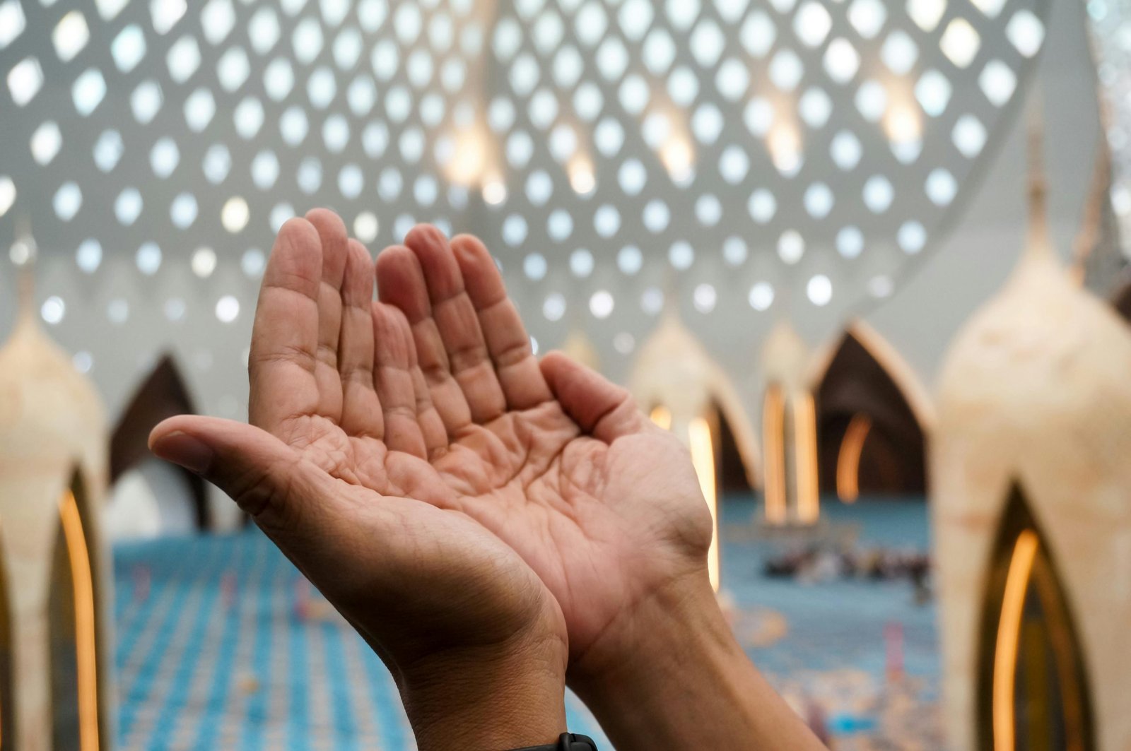 Hands raised in prayer within a beautifully lit mosque interior, symbolizing devotion.
