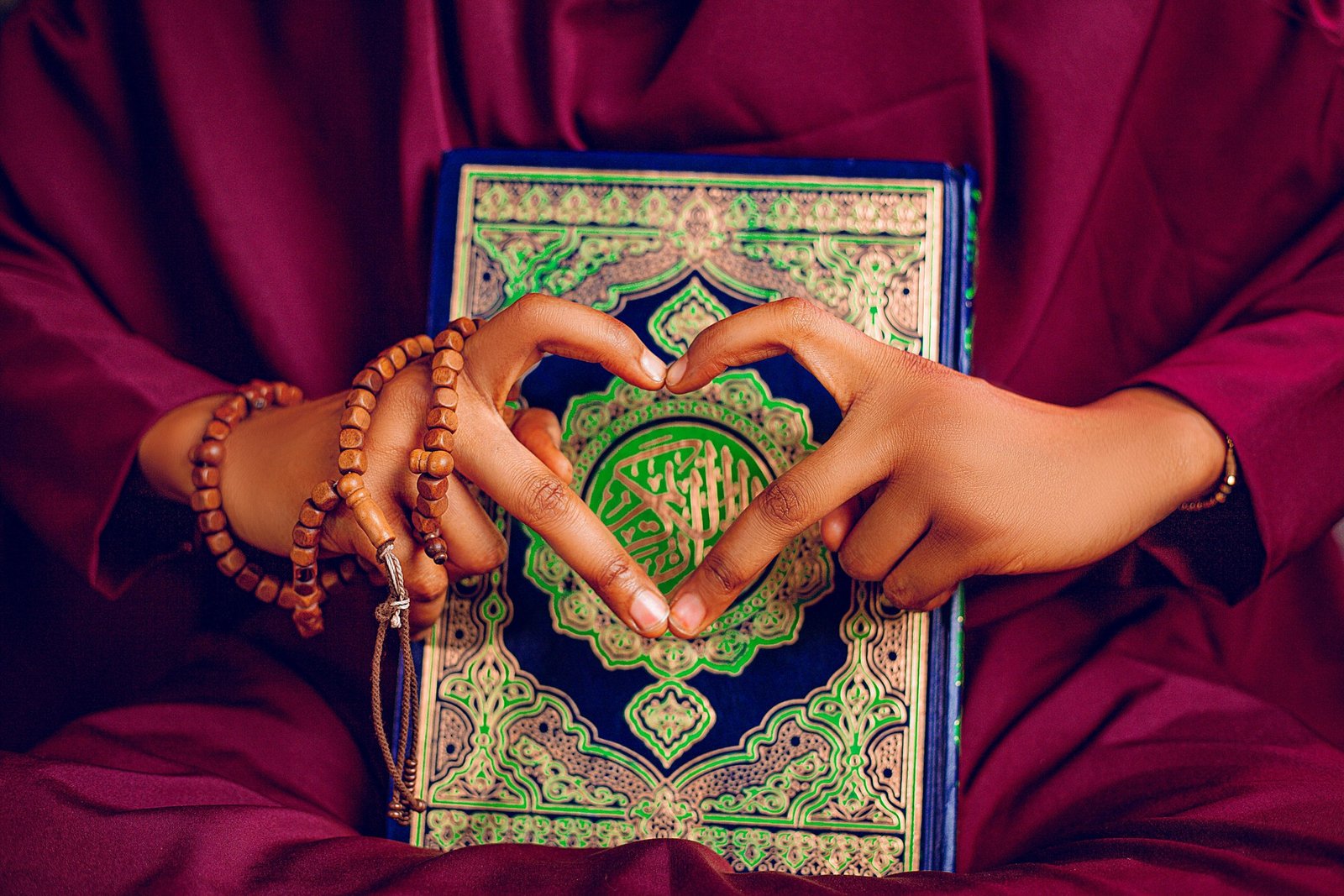 Hands form a heart over a beautifully adorned Quran, showcasing faith and devotion.