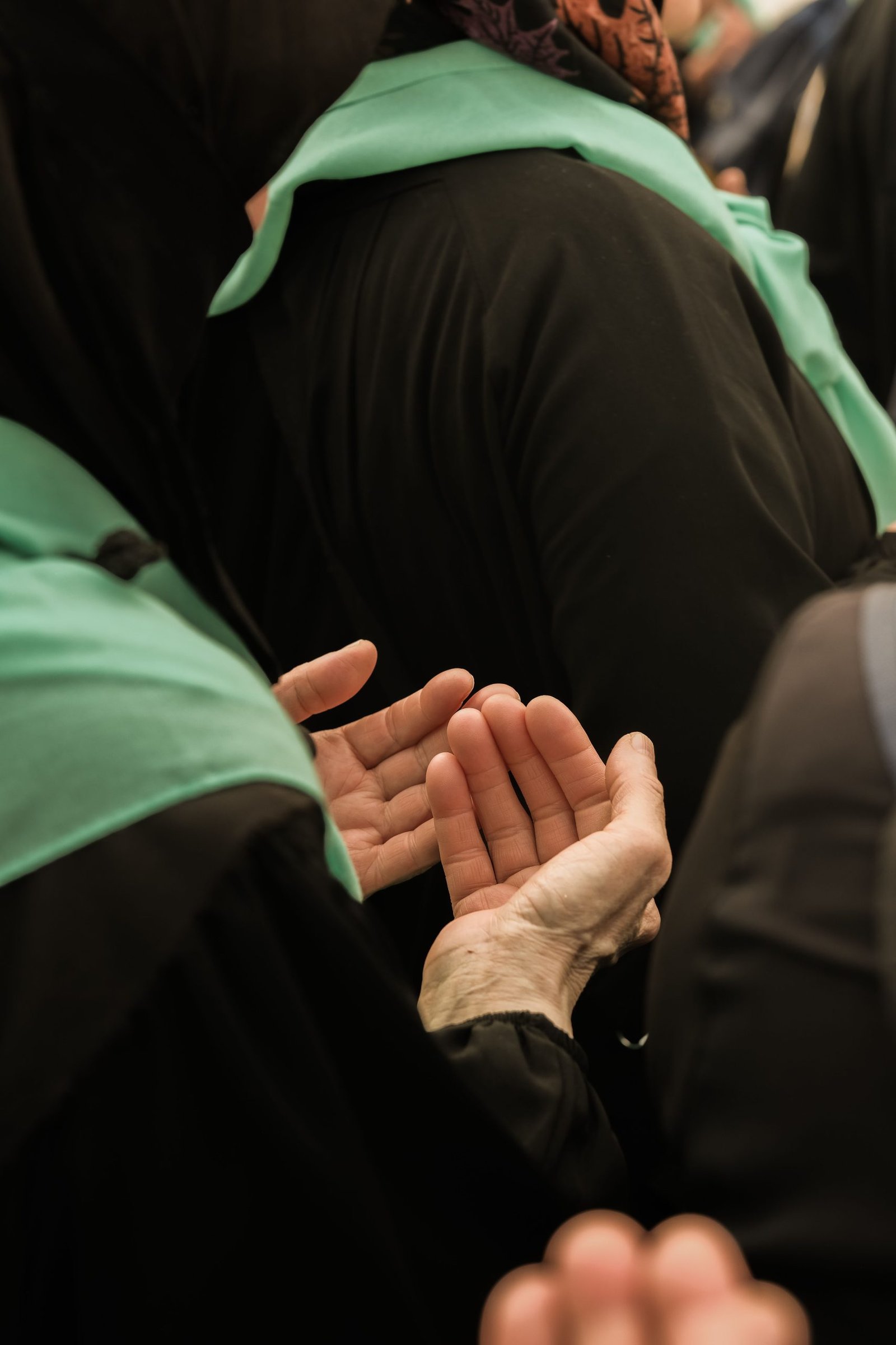 Middle Eastern women in traditional clothing praying with open hands during a religious gathering.